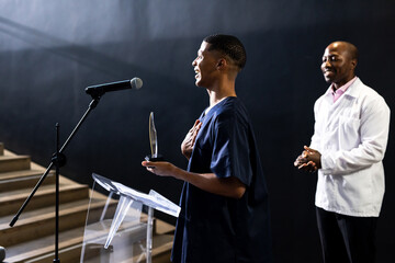 man holding award speaking at podium, smiling with pride, at conference hall