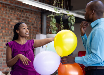 Diverse colleagues discussing event setup while holding colorful balloons in office