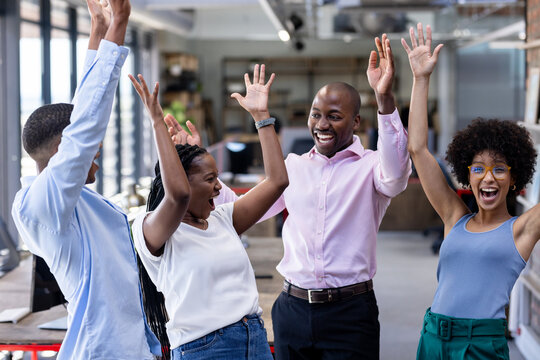 Diverse business diverse team celebrating success with raised hands in modern office