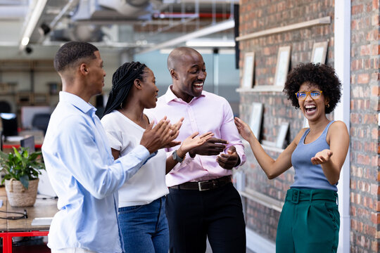 Celebrating success, diverse colleagues smiling and clapping in modern office