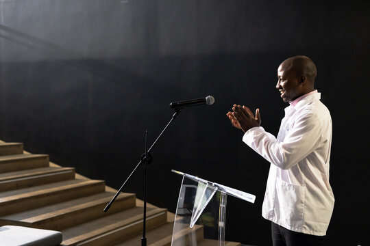 Businessman clapping hands at podium during presentation in modern conference hall, copy space