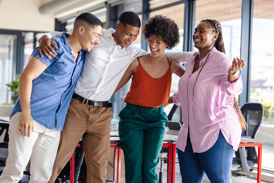 Laughing and embracing, diverse colleagues celebrating teamwork success in modern office