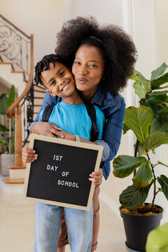 African American mother hugging son holding 1st Day of School sign, both smiling