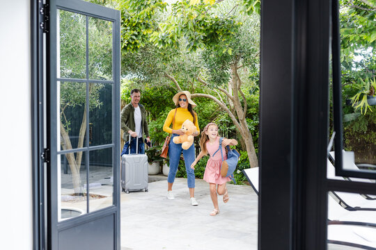 Family arriving at vacation home, carrying luggage and smiling with excitement