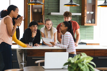 Diverse teens celebrating in kitchen, sharing exciting news and enjoying togetherness, at home