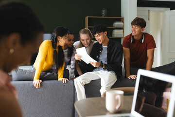 Diverse teens gathered on couch, reading college acceptance letter, celebrating success, at home