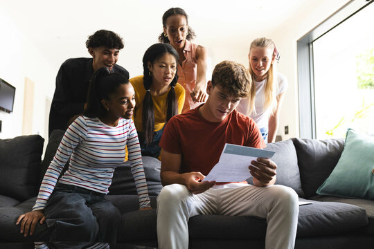 Reading acceptance college acceptance letter, diverse teenagers celebrating success on couch at home