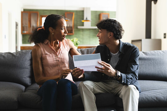 Celebrating success, teen showing acceptance college acceptance letter on living room couch, at home
