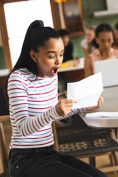 Reading college acceptance letter at school, teen girl in showing surprise and excitement, at home