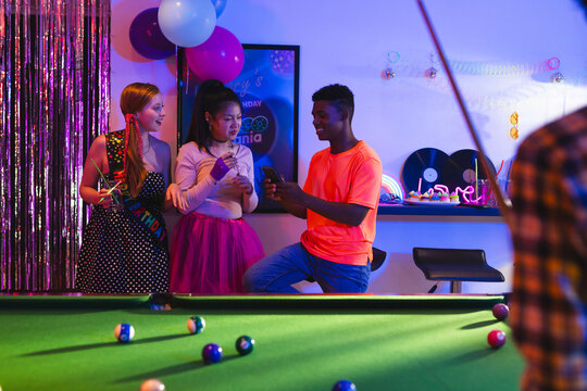 Teenage diverse friends celebrating birthday party playing pool and chatting in vibrant room, at hom