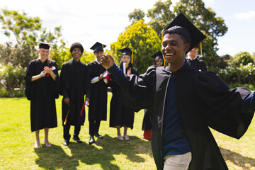 Teenage celebrating graduation in garden with diverse friends clapping and smiling in background