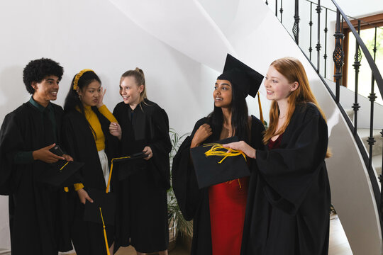 Graduating diverse students in caps and gowns celebrating together with joy and laughter, at home