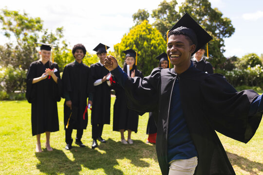 Teenage celebrating graduation in garden with diverse friends clapping and smiling in background