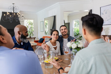 Friends enjoying conversation around dining table during small casual wedding celebration, at home