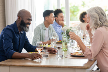 Friends enjoying laughter and conversation over dinner at small casual wedding celebration, at home