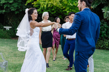 Bride and groom dancing joyfully on lawn with friends celebrating around them