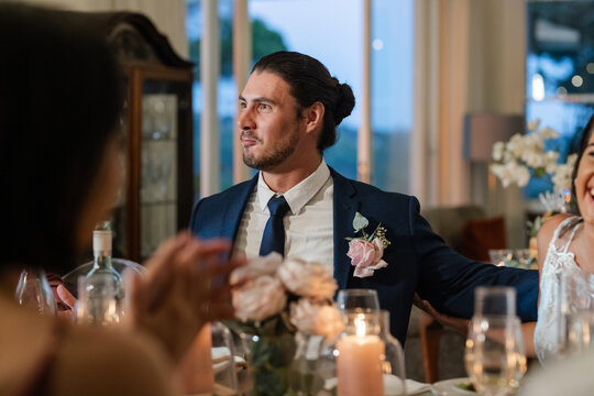 Groom in suit smiling at dinner table during wedding celebration indoors - Powered by Adobe