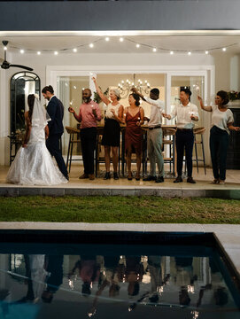 Celebrating by poolside, diverse group raising glasses, enjoying wedding reception, copy space