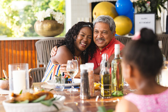 Diverse family celebrating retirement, daughter hugging father at dinner table, in garden