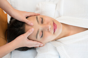Smiling female receiving facial massage or spa treatment. Woman lying down on white table with closed eyes and enjoying forehead massage © boonsom