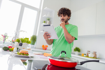 Young man in modern kitchen consulting recipe on tablet while preparing healthy meal during a bright sunny day indoors