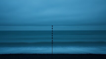 Obraz premium A solitary pole stands on a dark beach near the calm ocean