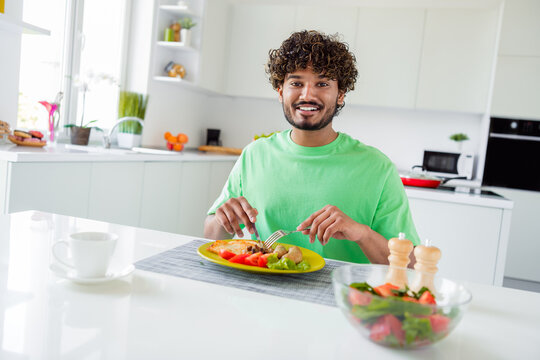 Smiling young man enjoying a healthy homemade meal in a bright modern kitchen during a cheerful and relaxed moment. - Powered by Adobe