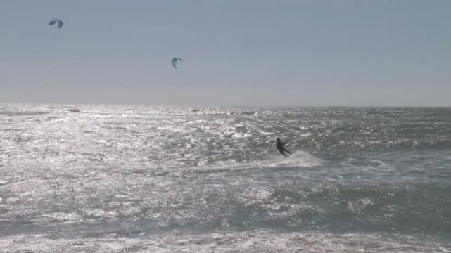 Kitesurfers glide over the waves enjoying on a windy day at the Canos de Meca, a wild, scenic beach along Vejer de la Frontera's coast in Cadiz, Andalusia, Spain.