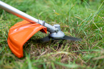 Cutting overgrown grass with a new trimmer in a backyard. New trimmer revs up as blades spin,...