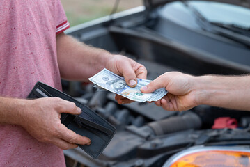 Payment with dollar money for car repair in a garage. Man driver pays cash for car repairs, with a...