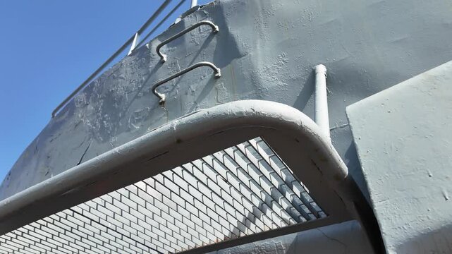 Low-angle view of a metal safety platform with grated surface and vertical ladder attached to the side of a ship, under bright daylight.