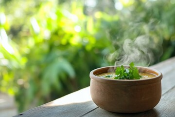 Steaming vegetable soup in clay bowl with cilantro on rustic wooden table.