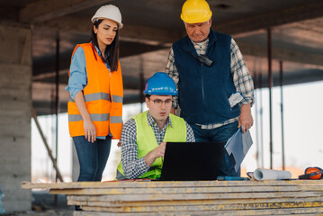 Construction workers analyzing blueprint on laptop at building site
