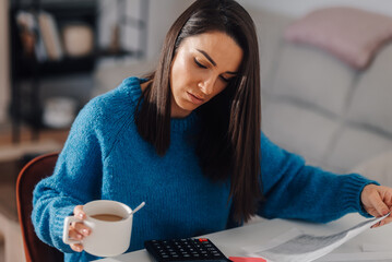 Woman drinking coffee and managing home finances with calculator and documents