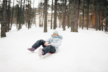Fototapeta premium Child sliding with sled in snowy forest during winter day