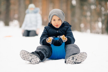 Happy child sliding on snow with sled in winter forest