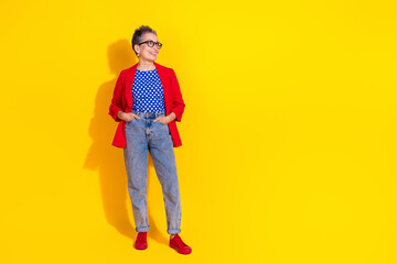 Fototapeta premium Stylish mature woman in red blazer and casual jeans posing joyfully against a vibrant yellow backdrop, expressing charm and elegance