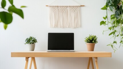 Laptop with blank screen sits on light wood desk, flanked by potted plants, against a white wall with macrame wall