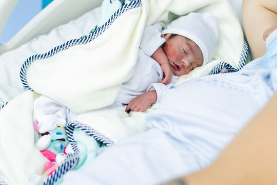 Newborn Latina baby in a hospital bed next to her mother. Her skin is still red and covered in vernix caseosa. A tender and emotional moment after birth, reflecting love and motherhood.