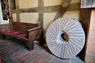 Old millstone with cutting pattern beside wooden pew in half-timbered mill