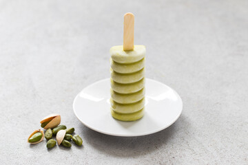 Pistachio ice cream on a wooden stick. On a plate. Light grey background
