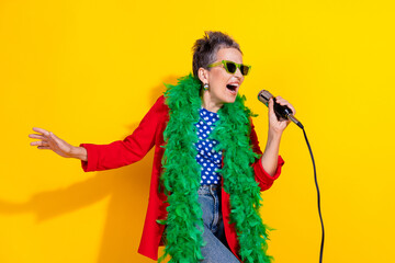 Middle-aged woman singing energetically with a microphone wearing vibrant glasses and a green...