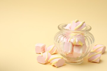 Tasty marshmallows in glass jar on beige background, closeup. Space for text