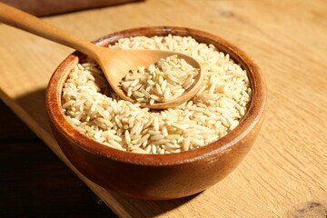 Brown rice and spoon in bowl on wooden table, closeup