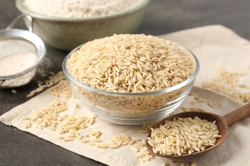 Brown rice, flour and sieve on grey table, closeup