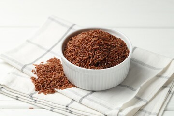 Raw brown rice in bowl on white wooden table, closeup