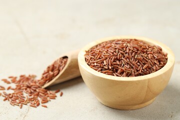 Brown rice in bowl and scoop on light grey table, closeup