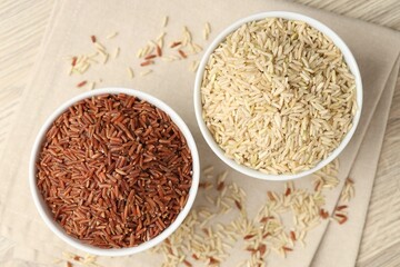 Different types of brown rice in bowls on wooden table, flat lay