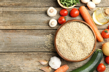 Raw brown rice in bowl among fresh products on wooden table, flat lay. Space for text