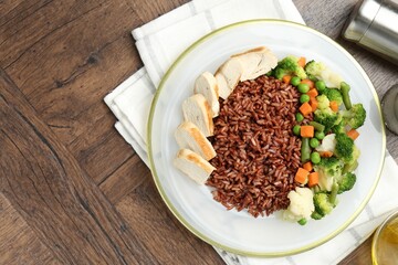 Delicious brown rice with chicken and vegetables served on wooden table, flat lay. Space for text